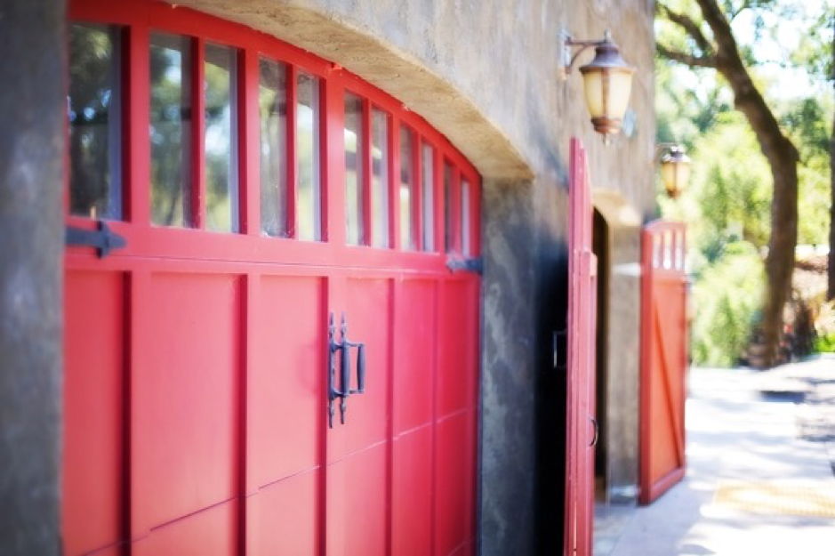 Two sets of red side hinged garage doors installed in a stone building 